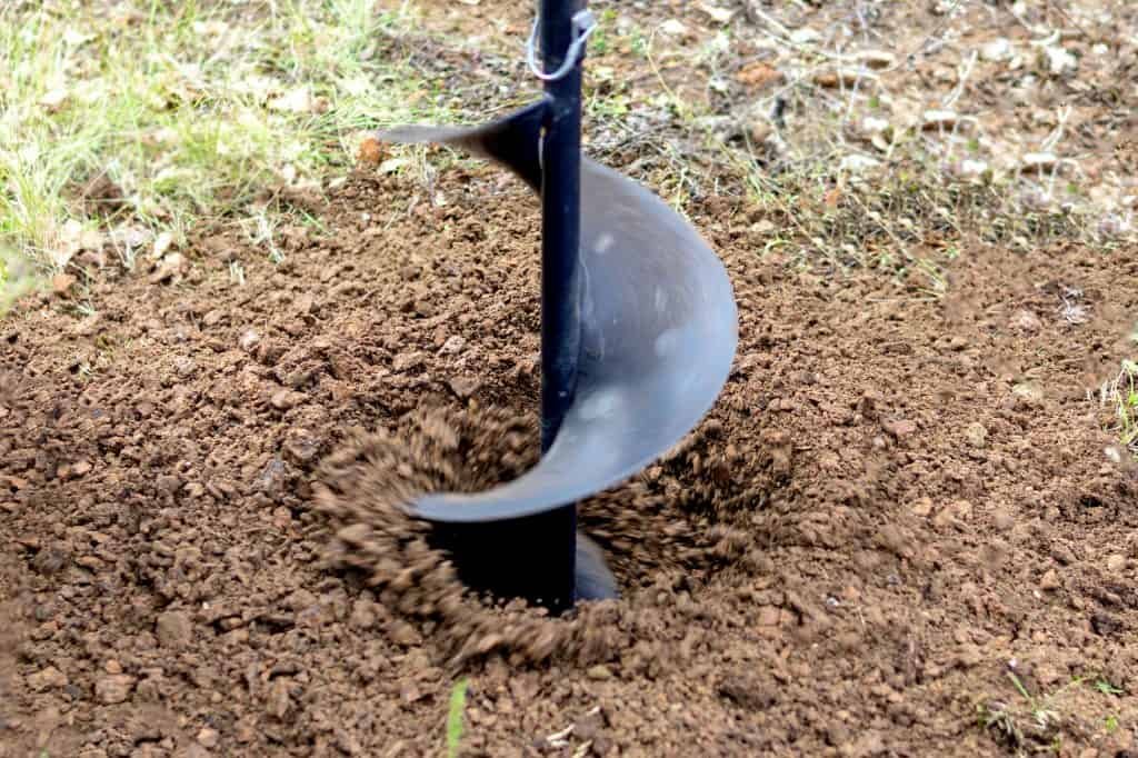 electric post hole digging a whole with dirt spinning off the auger