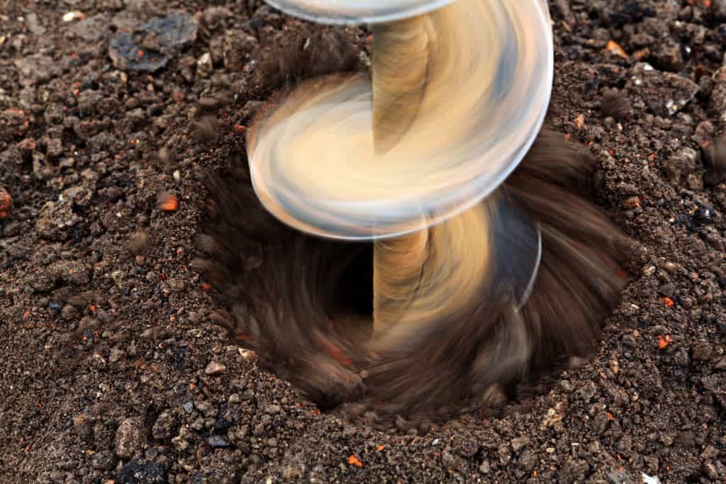 electric post hole digger digging hole in dirt