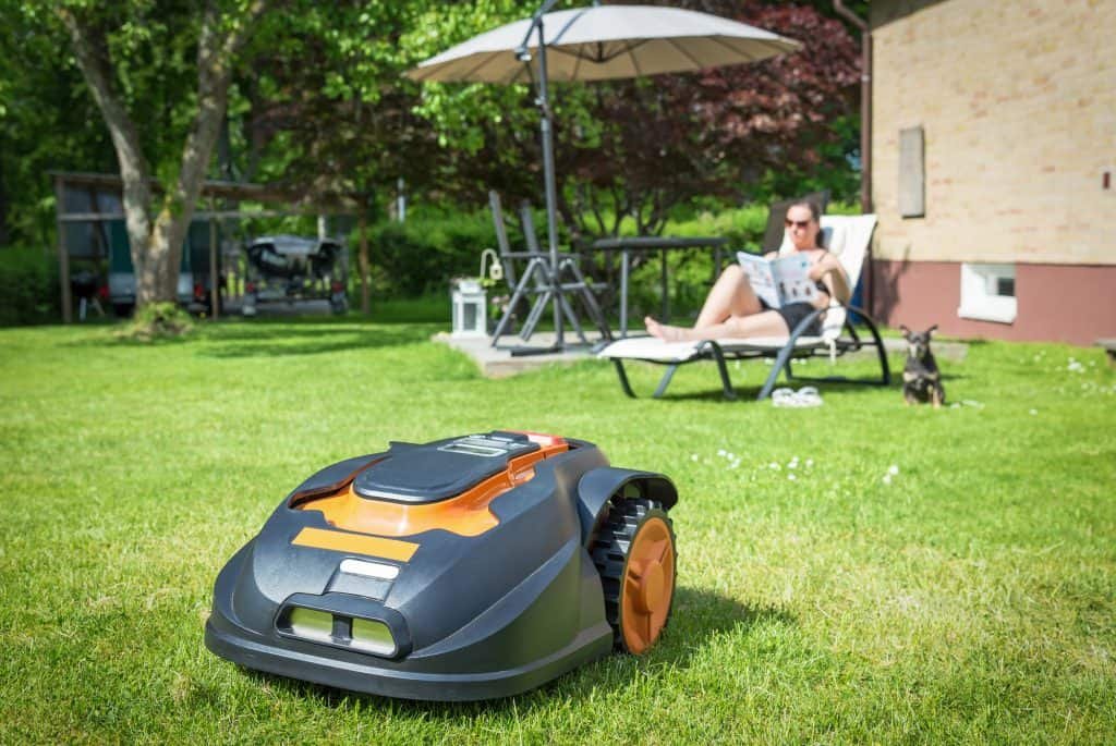 robot lawn mower cutting grass while woman sunbathes in backyard